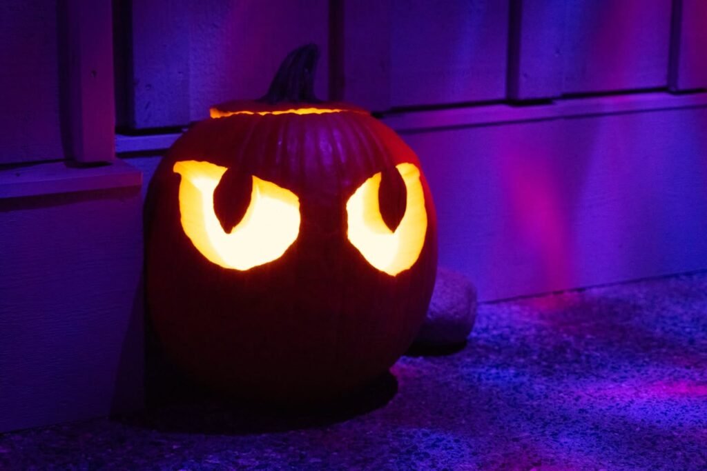 A carved pumpkin with glowing eyes and purple ambient lighting.