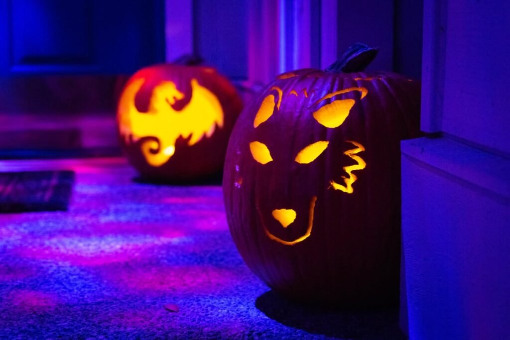 Two carved pumpkins illuminated by vibrant purple and blue Halloween party lights.
