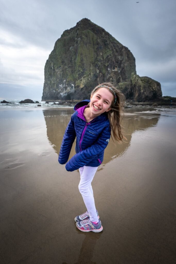 A person walks along a wet Pacific Northwest beach with a large coastal sea stack in the background.