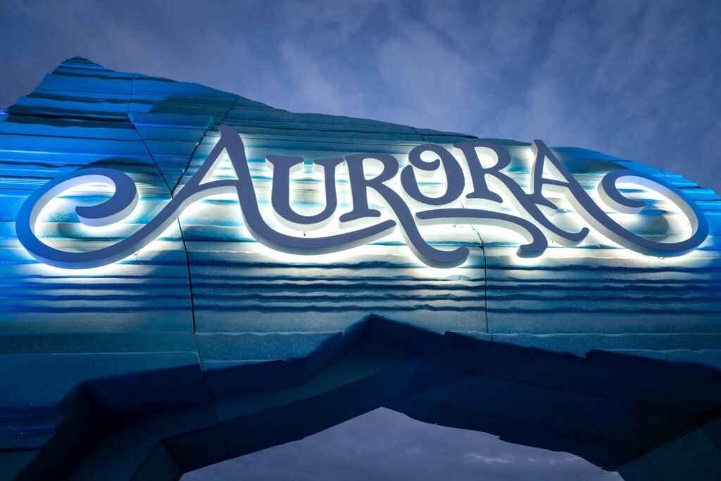 Close-up views of the illuminated Aurora sign on a curved, blue-striped fiberglass structure under a cloudy sky.