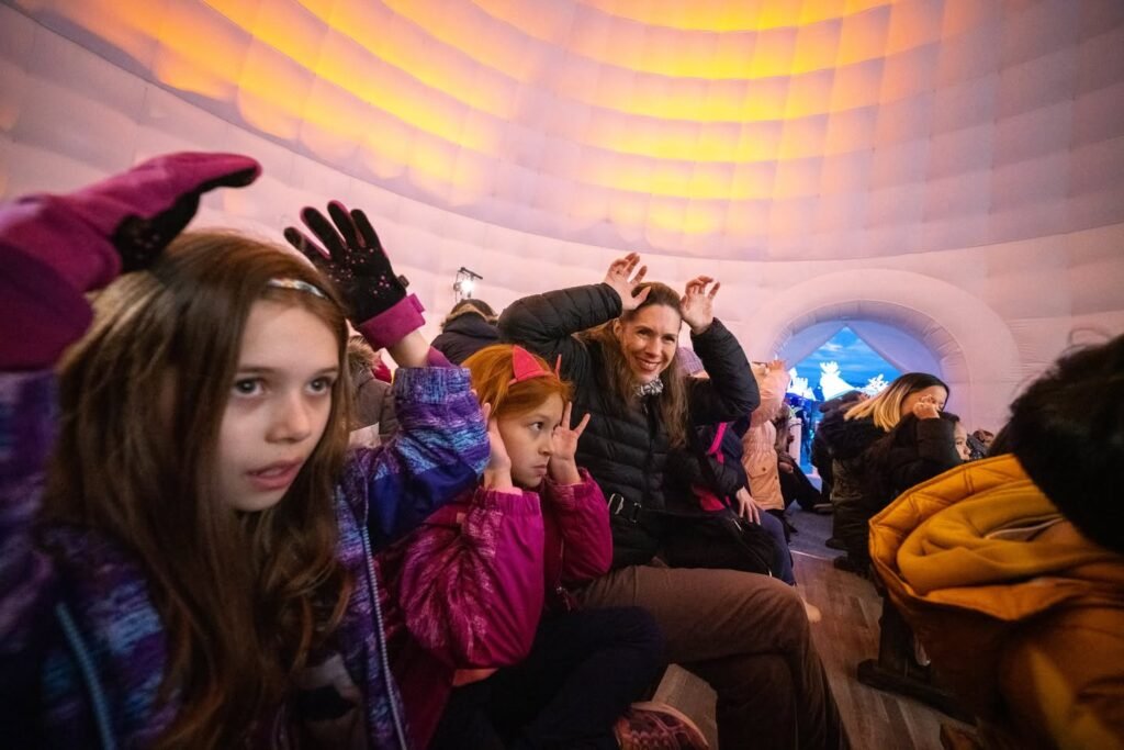 Guests explore a warmly lit ice hotel tunnel, reacting to the colorful interior and playful ice-carvings.