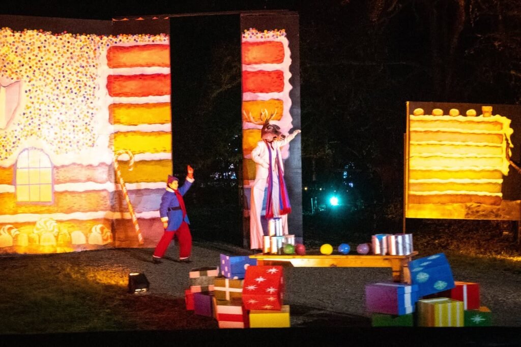 A vibrant nighttime display features two performers standing before illuminated installations of stacked, colorful rectangular panels.