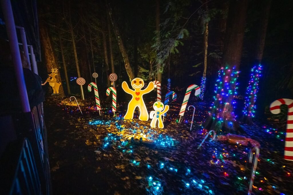 Colorful illuminated gingerbread figures and candy cane decorations in a nighttime forest setting.