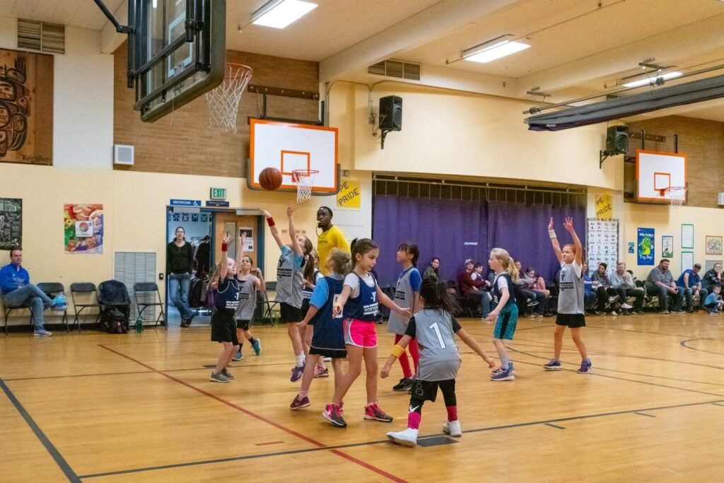 A youth girls basketball game in progress on a gymnasium court. The players are actively engaged in the game.