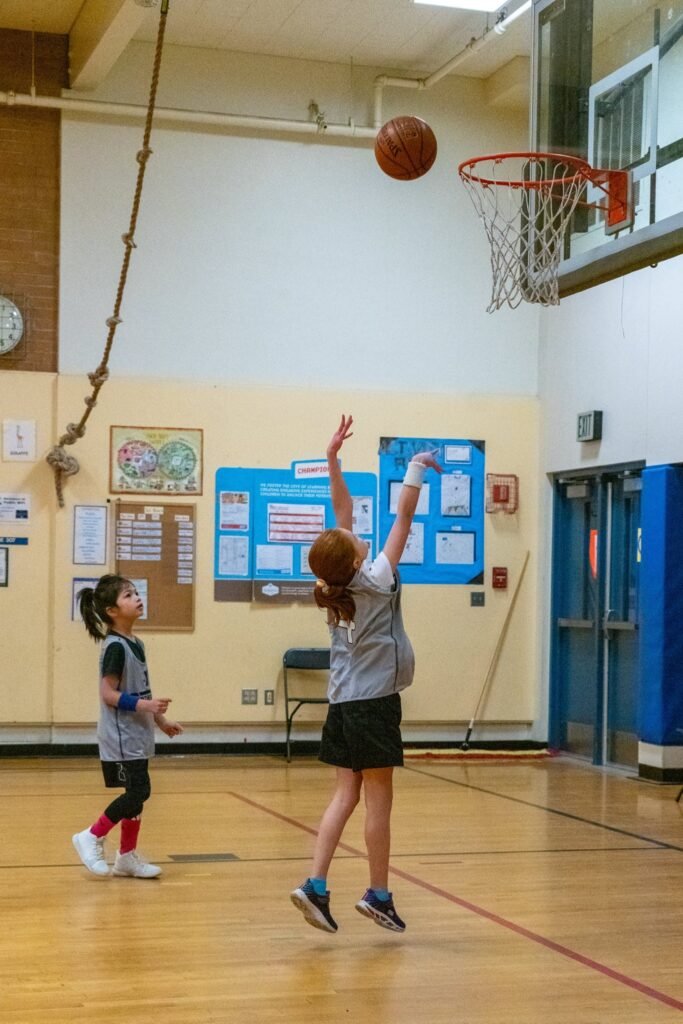A child shoots a basket in a school gymnasium while another watches.