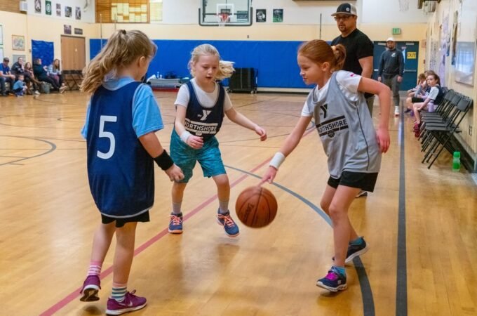 Children playing a youth basketball game inside a school gymnasium.
