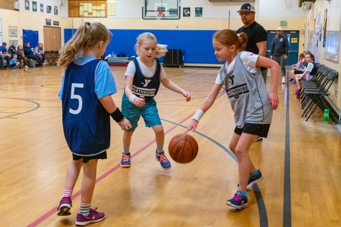 Children playing a youth basketball game inside a school gymnasium.