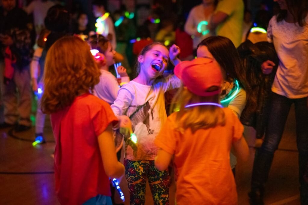 A group of children wearing glow sticks dancing at an indoor party.