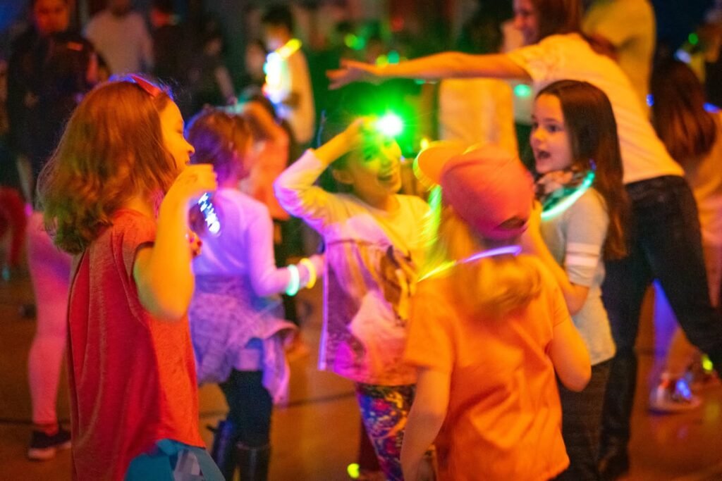 A group of children dancing under vibrant neon UV lights at a glow party.