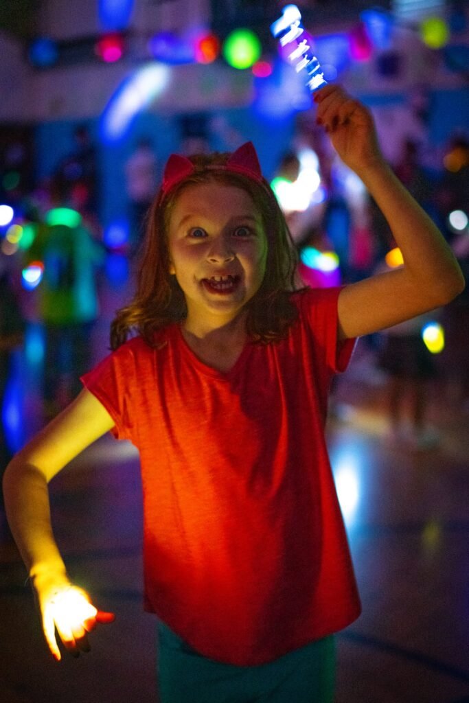 A child in a red shirt holding glowing light sticks with colorful bokeh lights in the background.