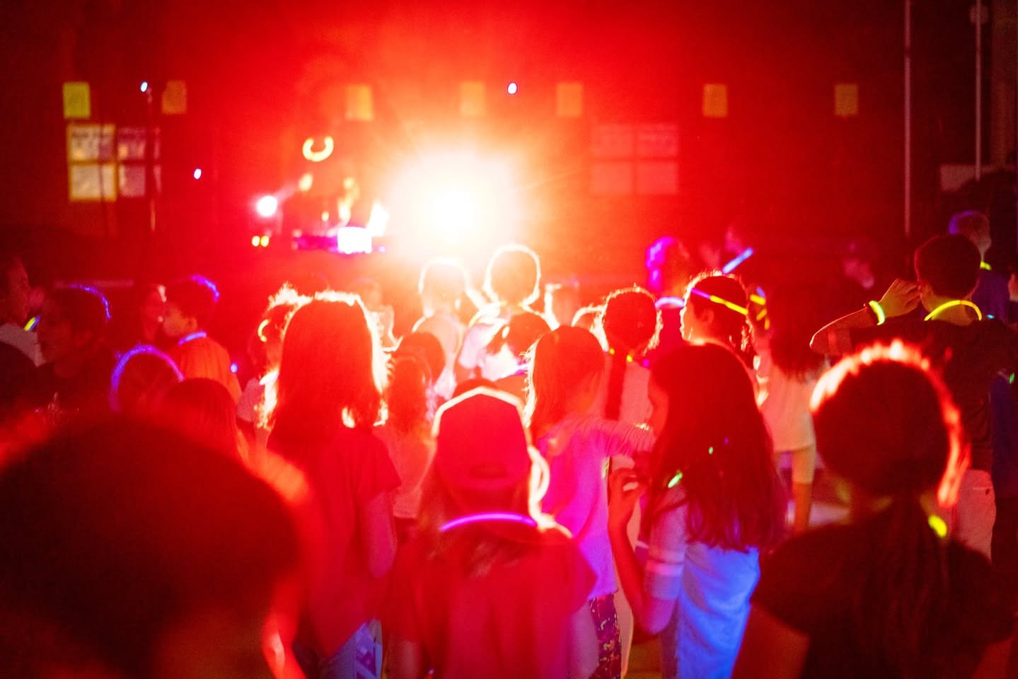Glow Dance An energetic audience at a concert, illuminated by intense red stage lights and a bright spotlight from the back.