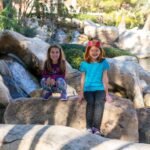 Visitors sitting and standing on large rocks near a waterfall.