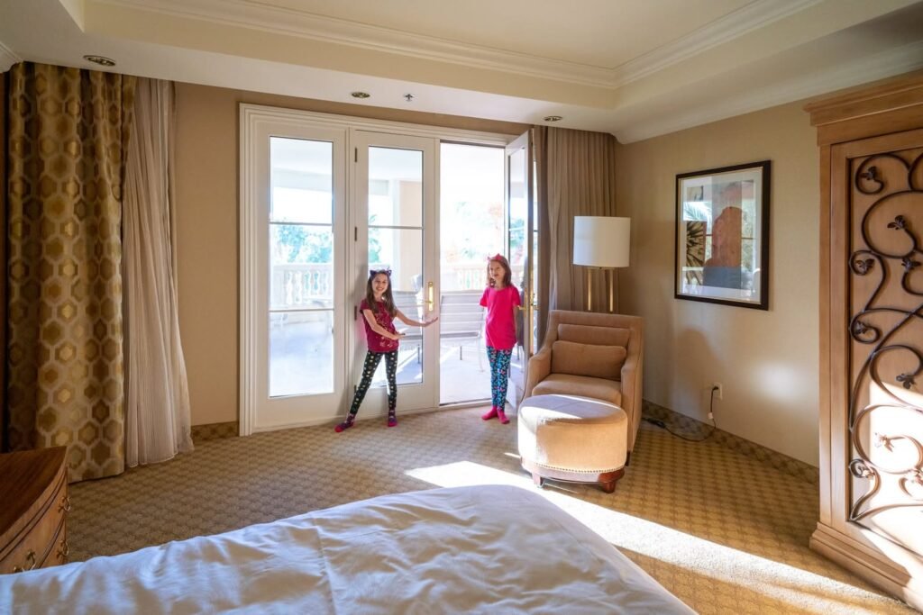 A spacious hotel room with a large bed, glass doors, and natural light where two guests are enjoying the hotel room.