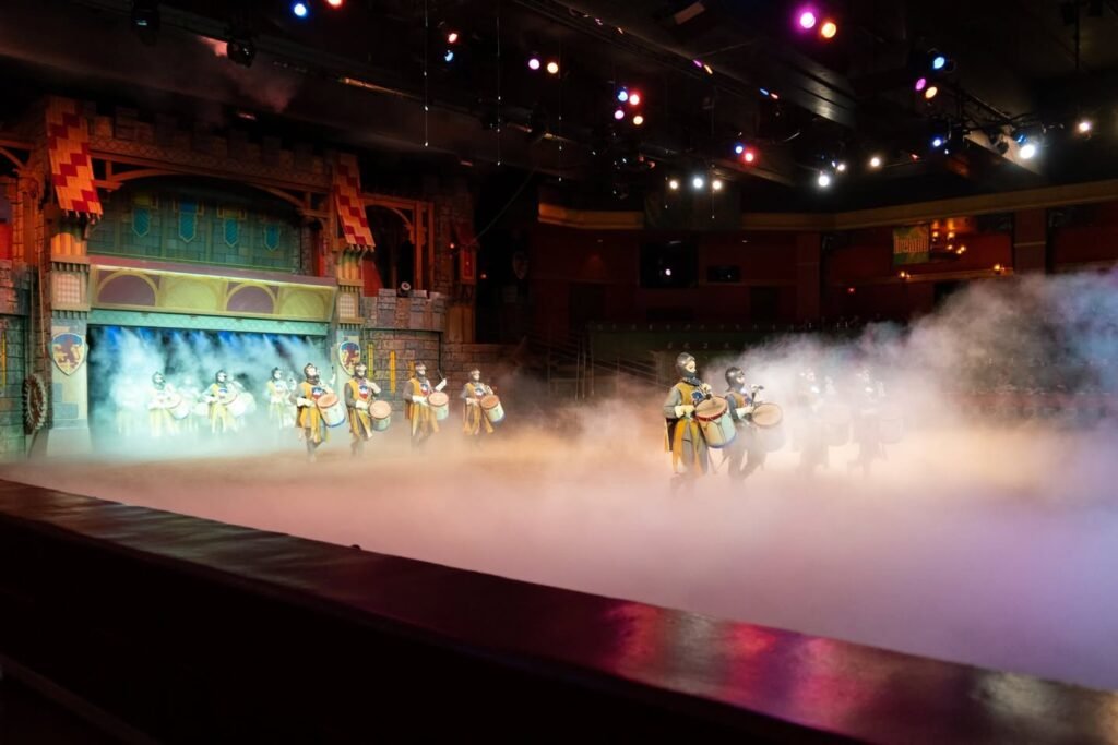 Cinderella's Royal Banquet show featuring cast members dancing on a stage enveloped in atmospheric fog effects, with detailed set design and lighting.