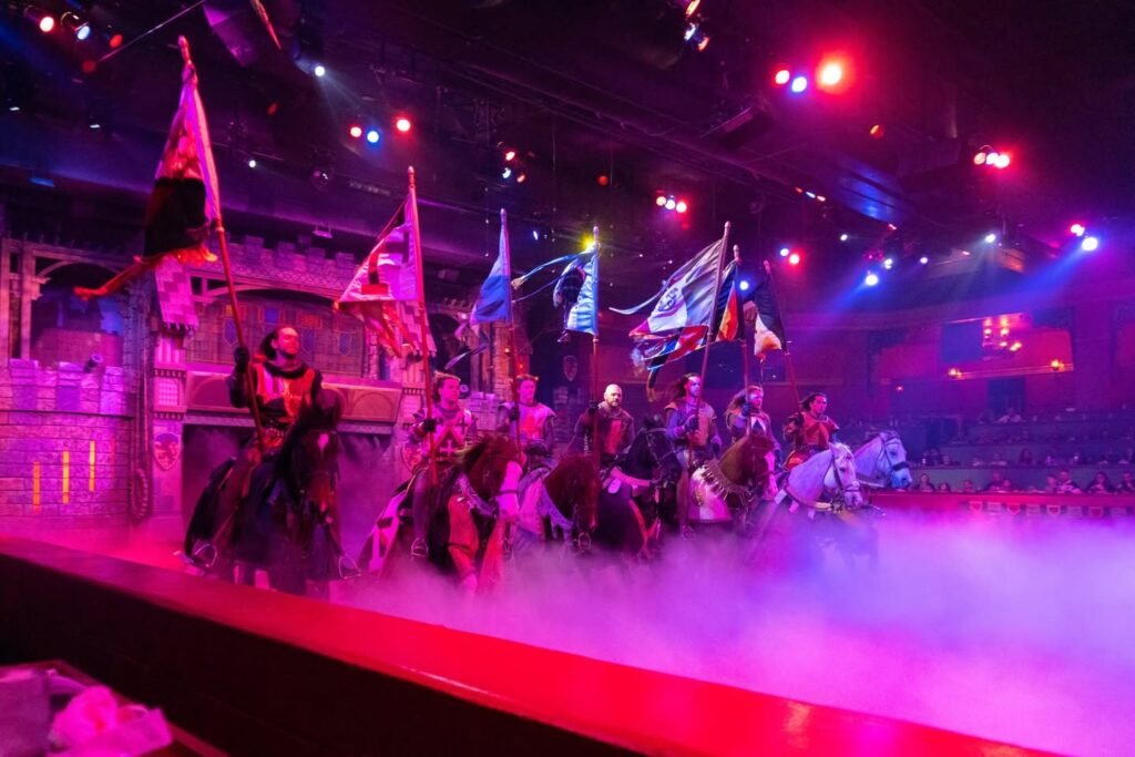 A dramatic Viking ship with horses and performers under pink and purple stage lights.