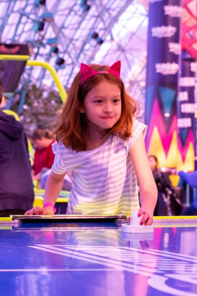 A child wearing a striped shirt and a red headband plays a game in an indoor arena with colorful decor.