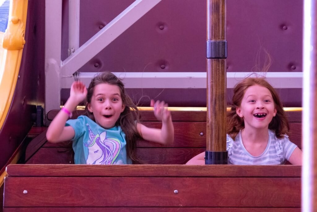 Two smiling people waving from a wooden carnival ride with a purple ceiling.