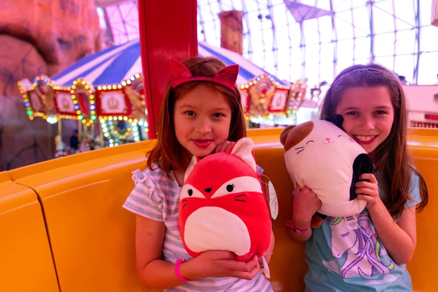 Circus Circus Children holding plush toys at a carnival ride, with carousel lights in the background.