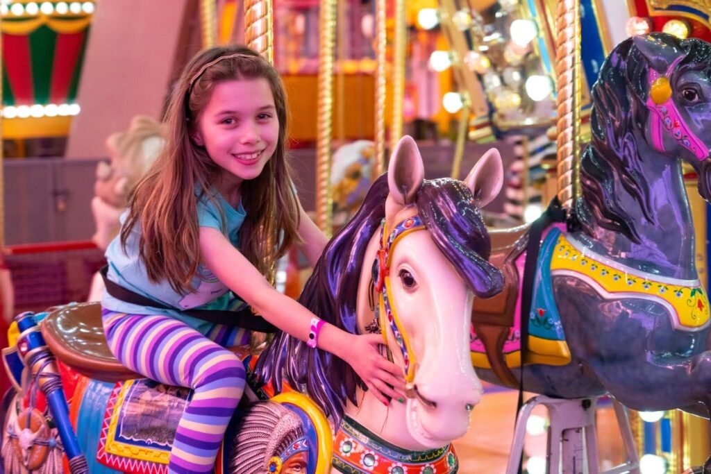 A young girl smiles brightly while riding a colorful horse on a carnival carousel.