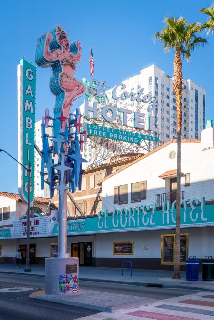 A sign for the El Cortez Hotel in Pacific Beach with a mermaid statue displayed against a bright blue sky and palm trees.