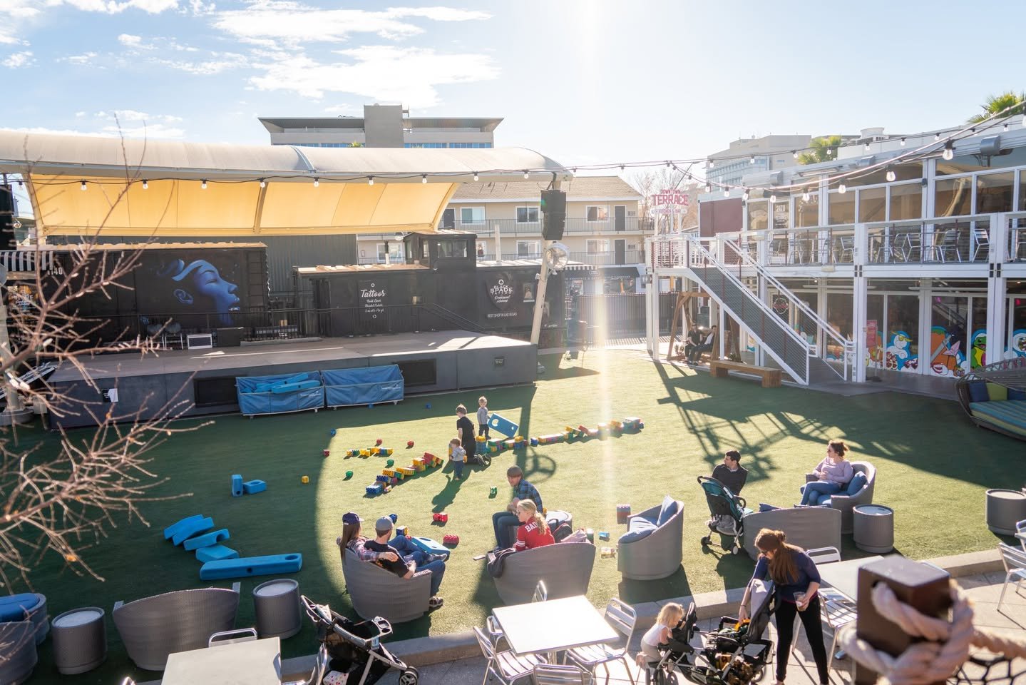 Container Park A lively rooftop space with a grassy area, colorful play structures, and outdoor seating. People are relaxed on the lawn, with the city skyline visible in the distance.
