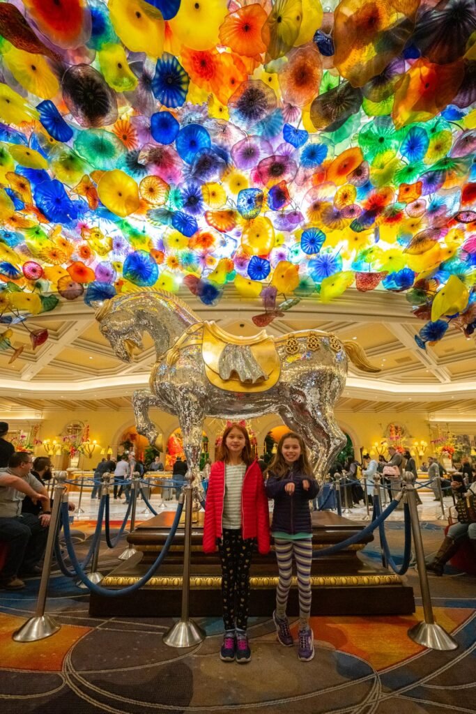 Two children standing under a colorful stained-glass chandelier in a grand lobby.