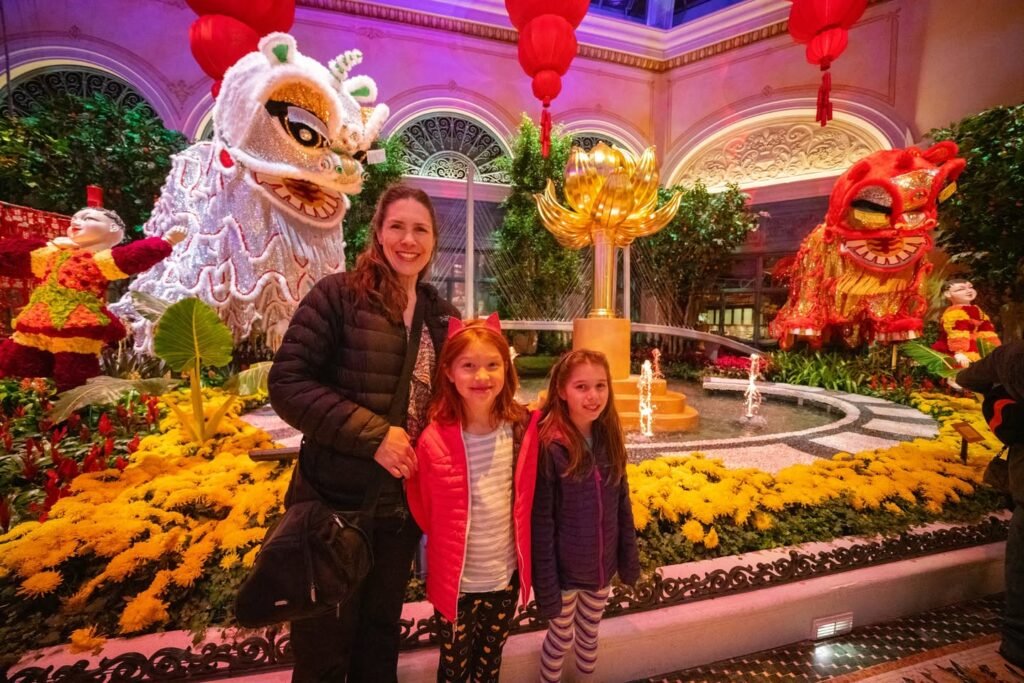 A family poses in front of vibrant floral displays and traditional Chinese lion statues in an indoor garden setting.