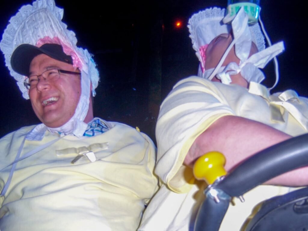 Two individuals wearing French beret-style bags on their heads and dresses while riding an amusement park ride at night.