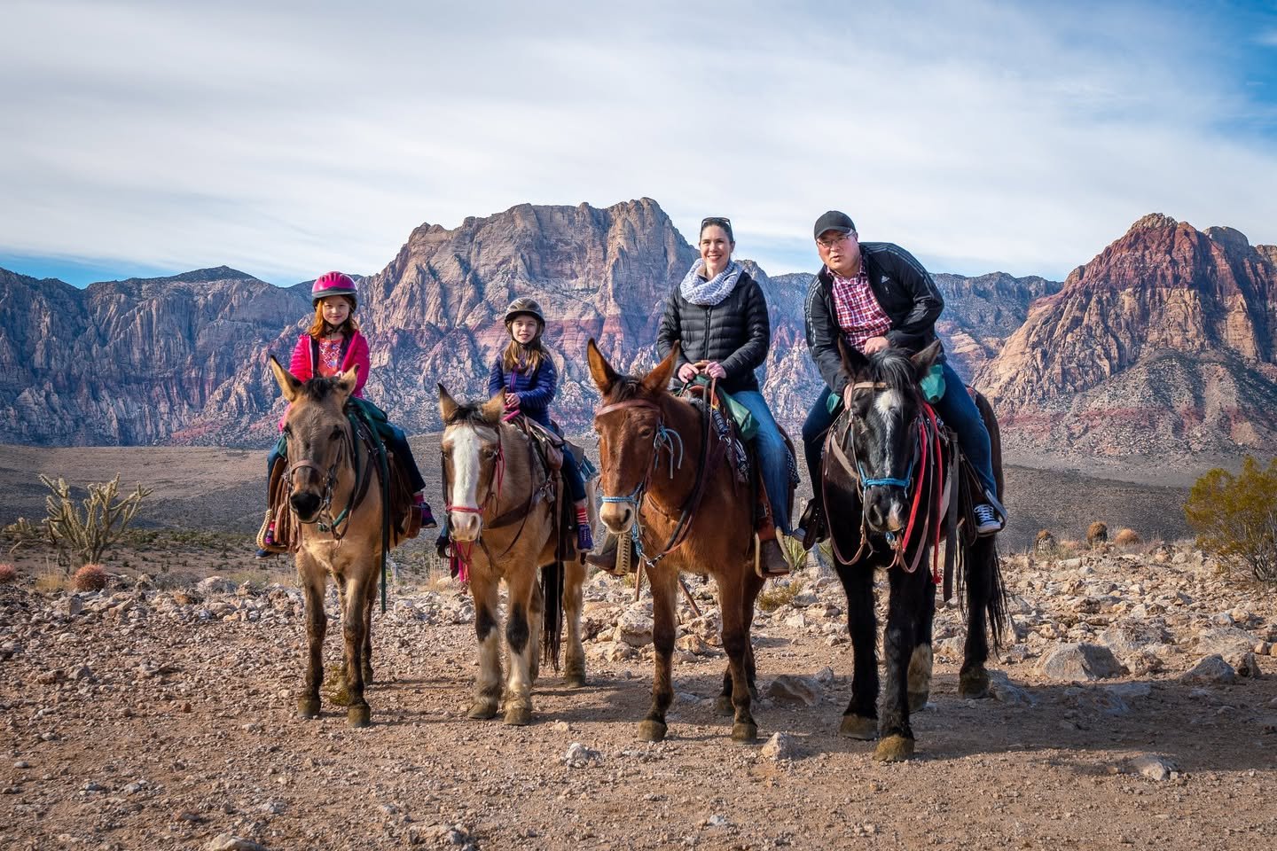 A group of people riding donkeys along a rocky trail with a backdrop of rugged mountains and desert terrain.