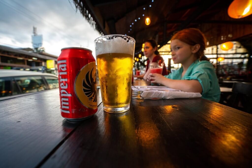 A red can of Imperm beer is next to a glass of beer and a beer glass.
