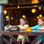 A curious cat lounges on a wooden table while two children observe at the Natural Market.