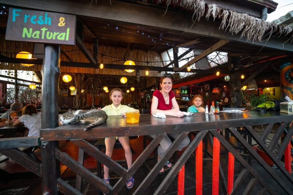 A family seated at a tiki-style bar with a sign reading Fresh & Natural. Warm lighting and rustic wooden decor create a fun atmosphere.