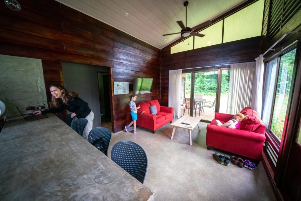 A cozy family room featuring dark wood walls, red sofas, and large windows overlooking lush greenery.