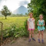 Horseback Riding at Club Rio Two hikers stand on a dirt path near lush green walls and distant volcanic peaks.