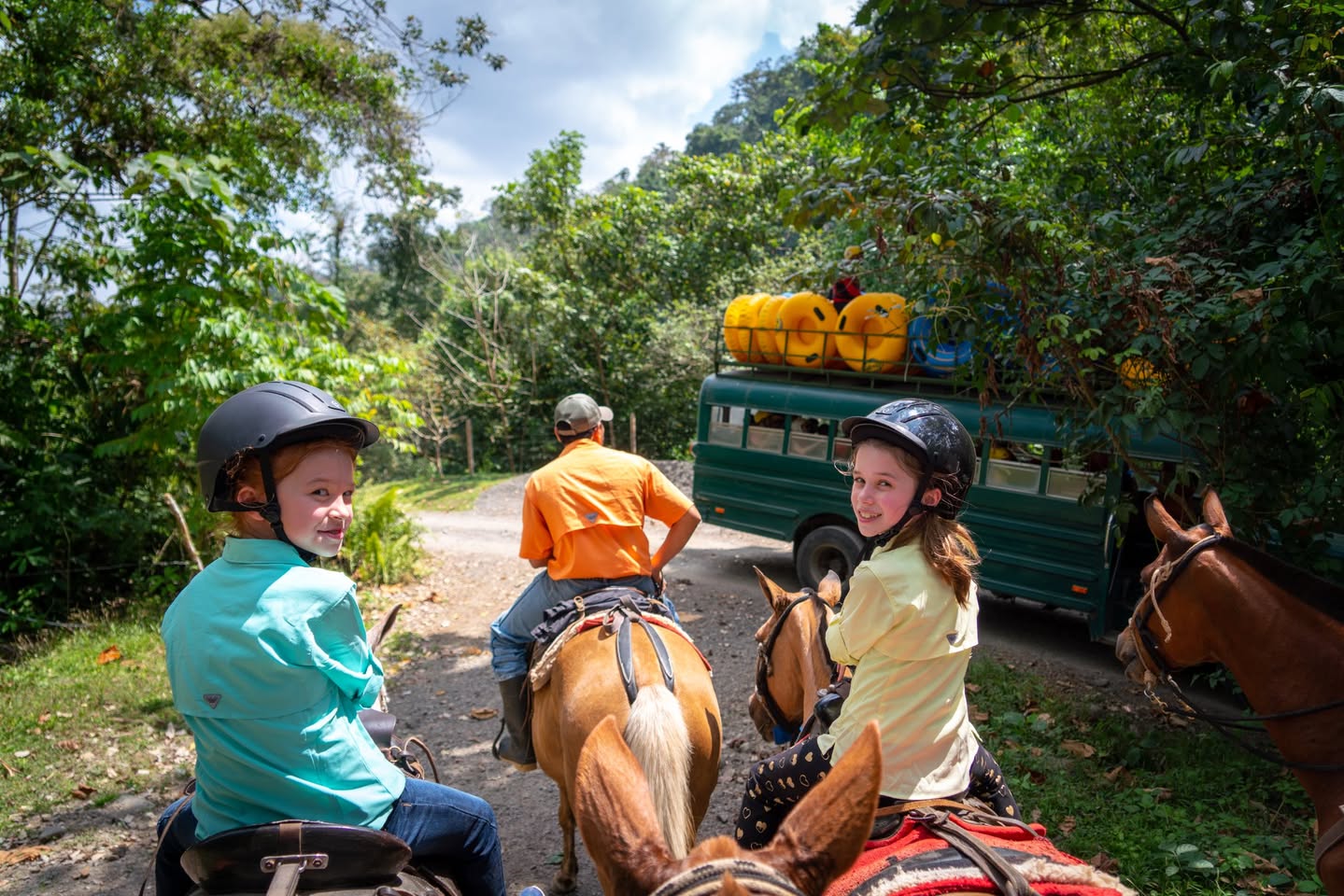 Horseback Riding at Club Rio Riders on horseback navigate a forest path with a loaded truck and vibrant greenery.