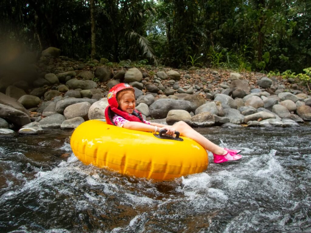 A person sits on a bright yellow inflatable tube floating down a rocky stream.