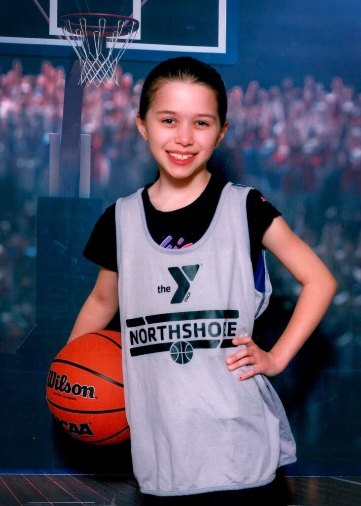 A young basketball player wearing a Wilson-branded jersey and holding a Wilson basketball in front of a hoop backdrop. The setting reflects an indoor studio photo shoot.