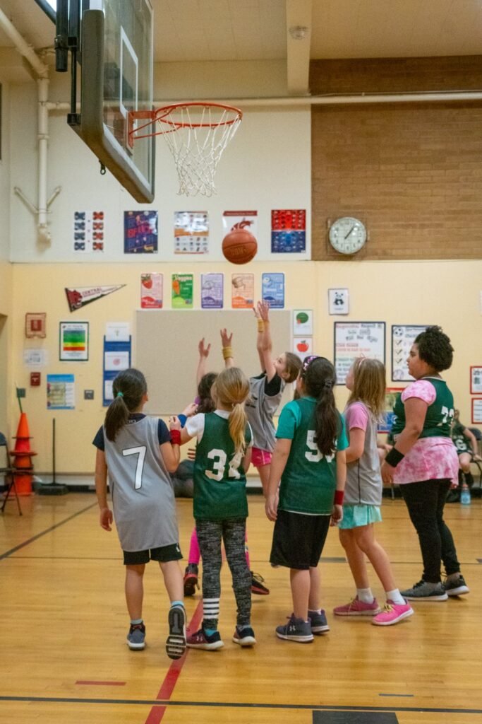Young athletes competing in an indoor basketball game in a brightly lit gymnasium.