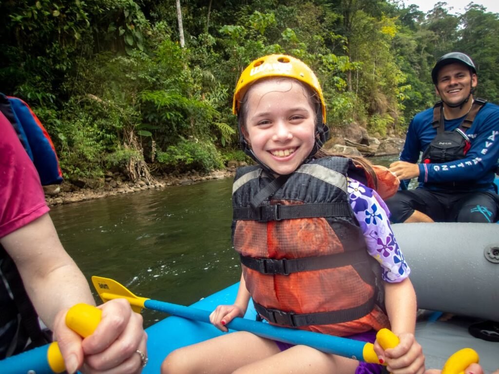 A family enjoys a river rafting adventure in a lush jungle setting, wearing safety helmets and life jackets.