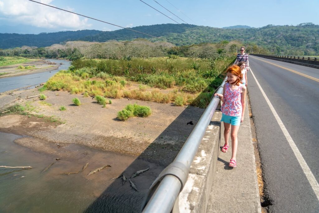 A child walks along the edge of a coastal highway with a river and mountains in the background, capturing a moment of exploration and adventure.