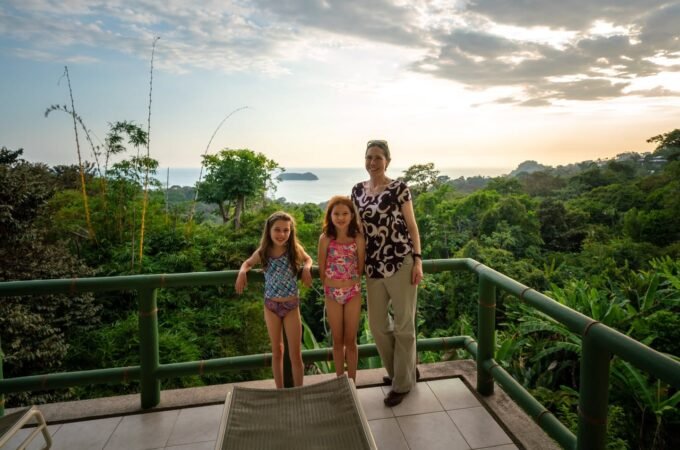 A family enjoys a ride on a swing overlooking a lush tropical forest and the ocean from a high vantage point.