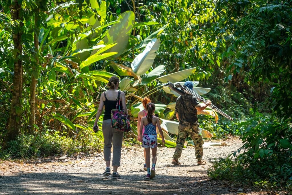 A family of three walking down a dirt path in a lush jungle setting. Lush green leaves and trees surround the trail.