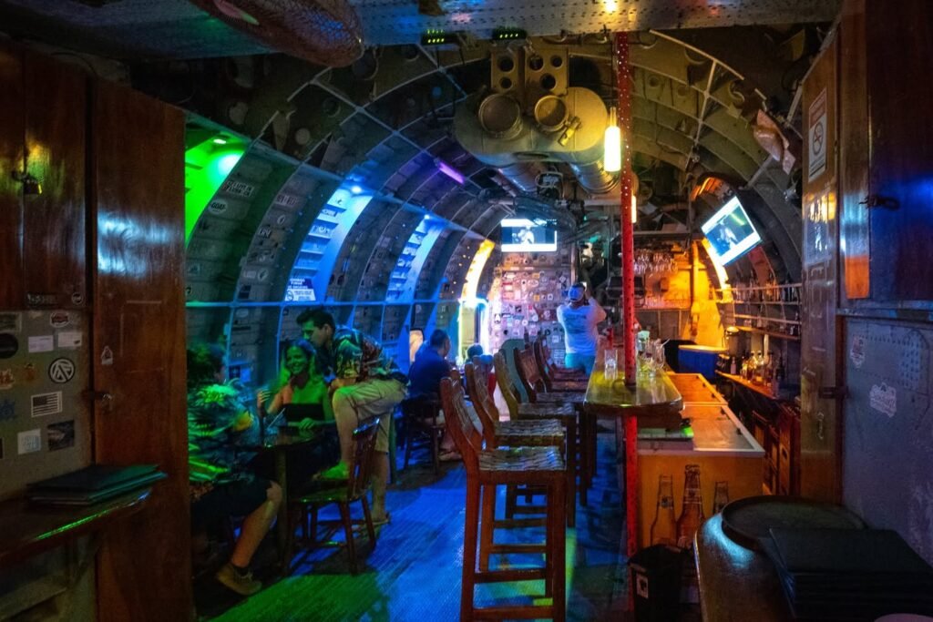 A narrow, colorful bar interior featuring wooden panels and unique lighting.