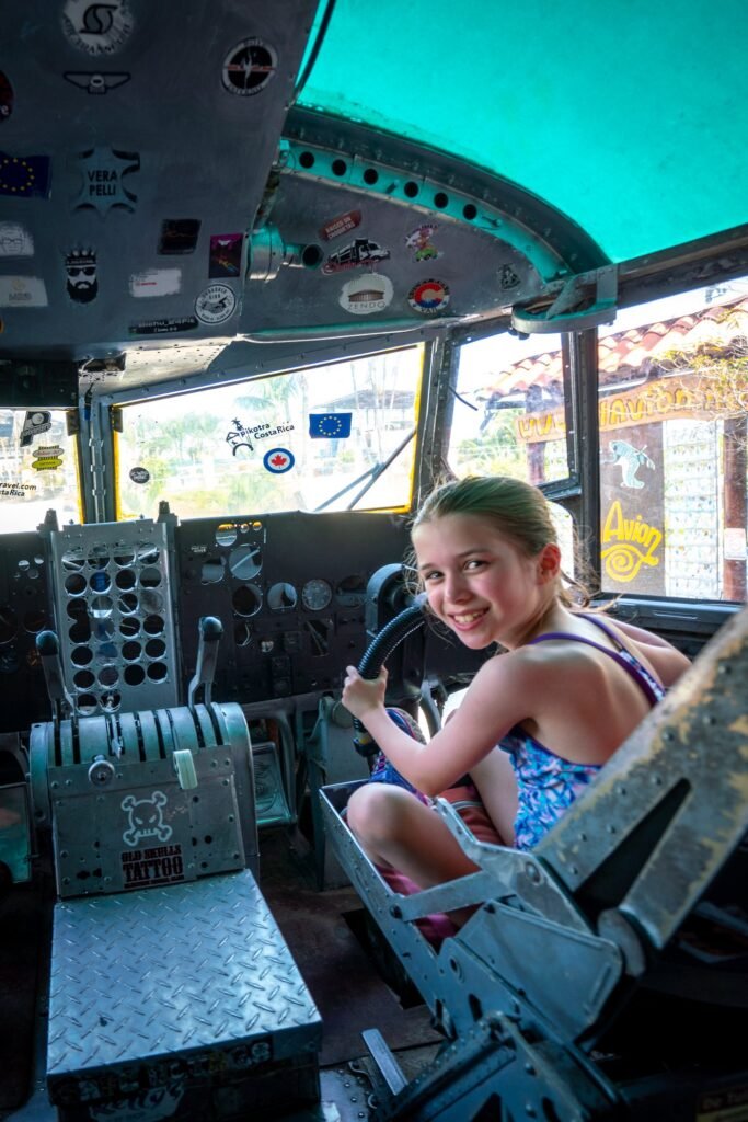 A young girl smiles while riding a Tilt-A-Whirl amusement park ride. The cockpit-like seat is surrounded by control panels and dials.