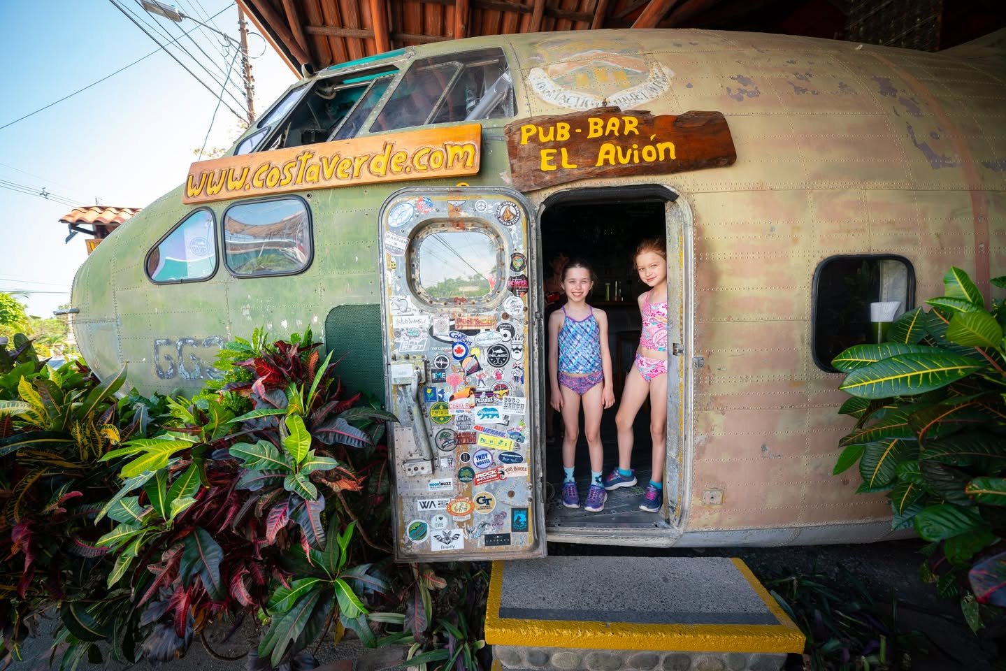 Stoppers stand in the doorway of El Avion, a distinctive airplane pub bar surrounded by tropical plants.