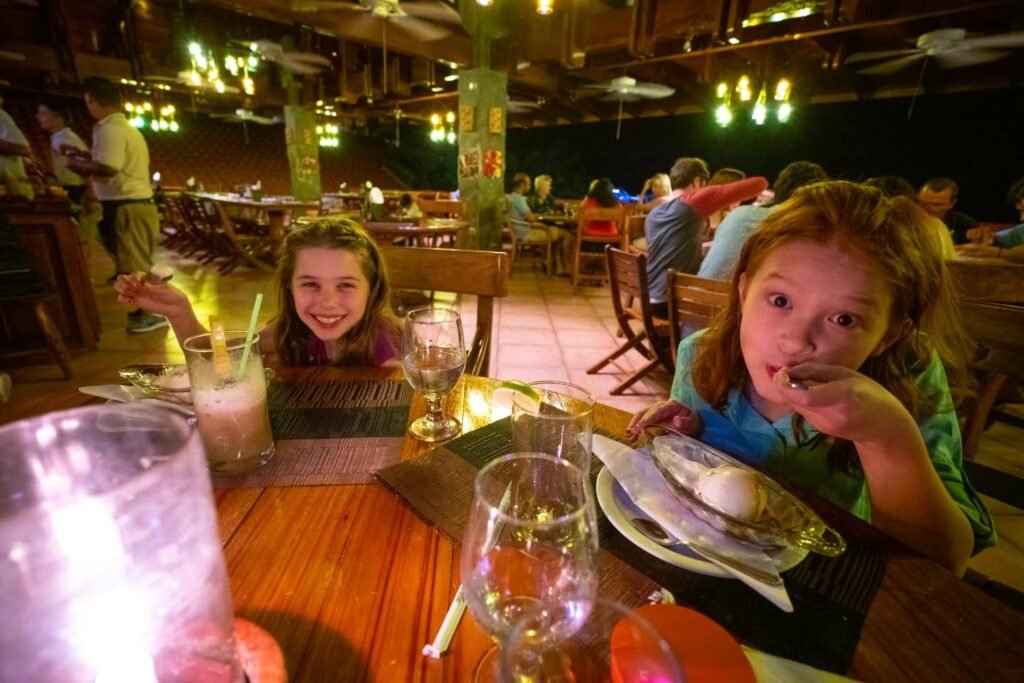 Children enjoying a meal at a tropical-themed restaurant with wooden tables and warm lighting.