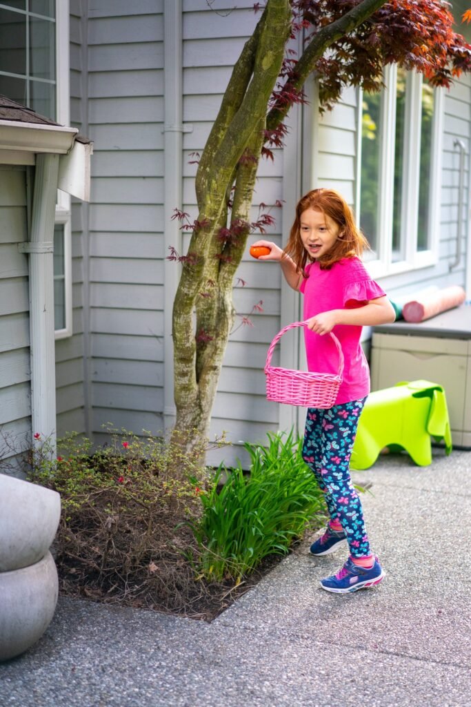 A child in colorful pajamas holding a pink Easter basket on a patio.