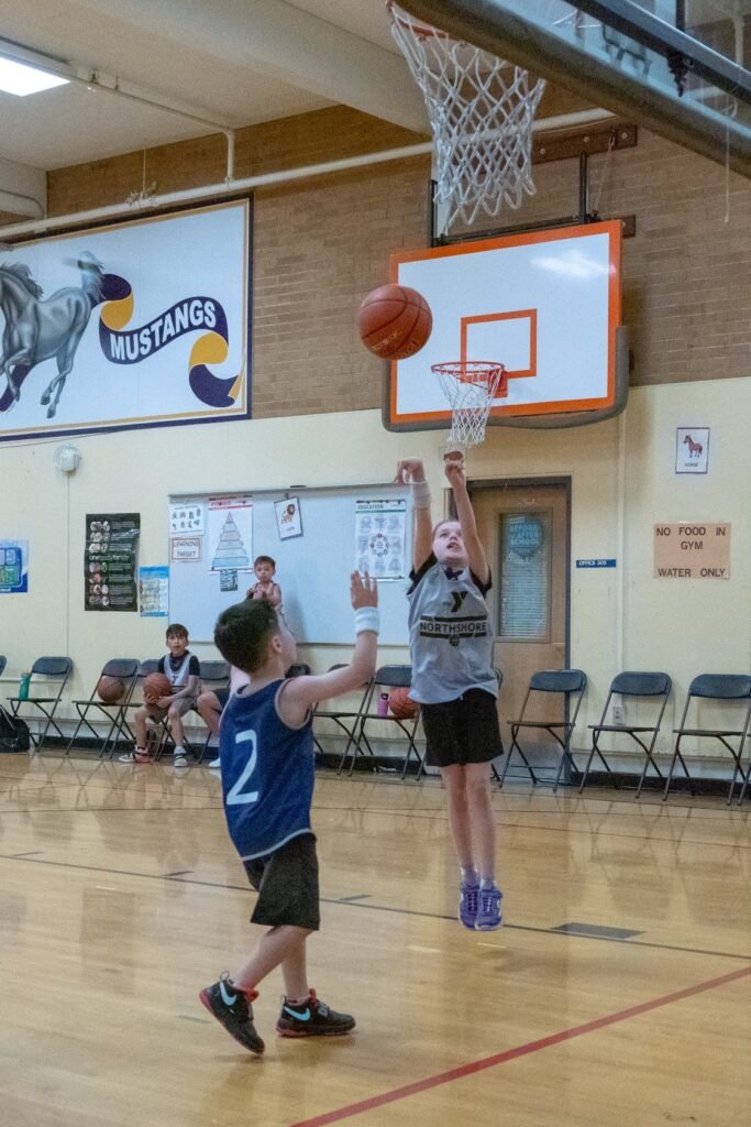 Child playing basketball in a gym with a 'Mustangs' banner in the background.