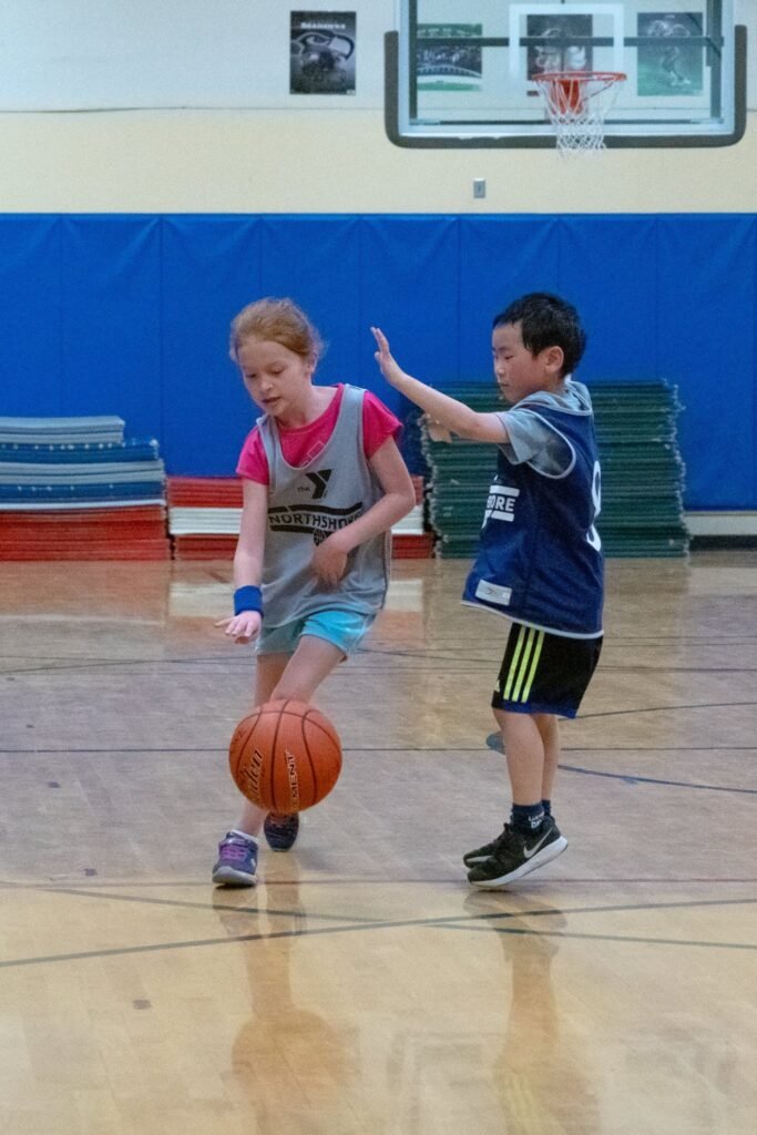 Children playing basketball indoors on a wooden court.