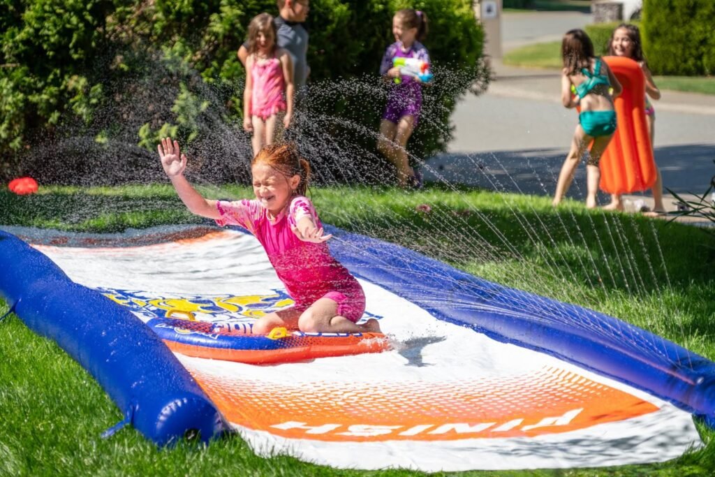 Children playing on an inflatable slip and slide in a backyard sprinkler setup.
